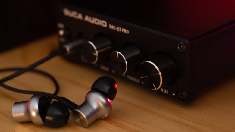 A headphone amplifier on a desk with in-ear monitors sitting next to it
