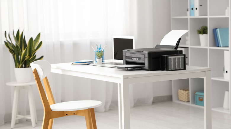 A black printer on a white desk in a home office.