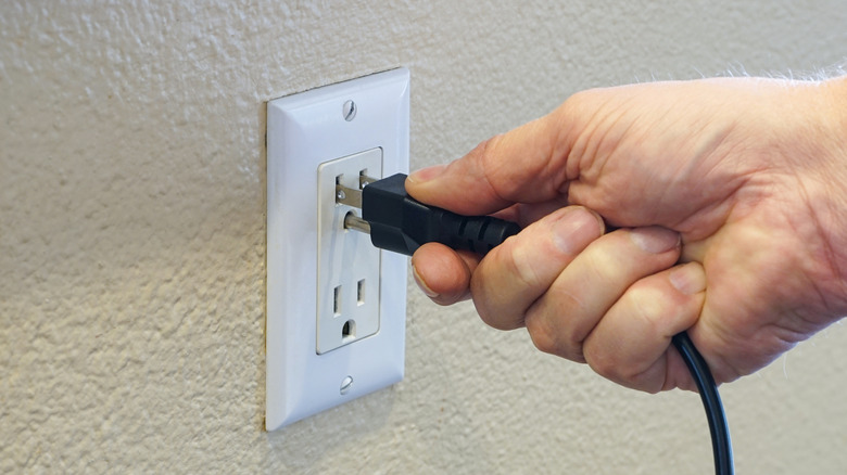Hand inserting 3-prong plug into wall outlet