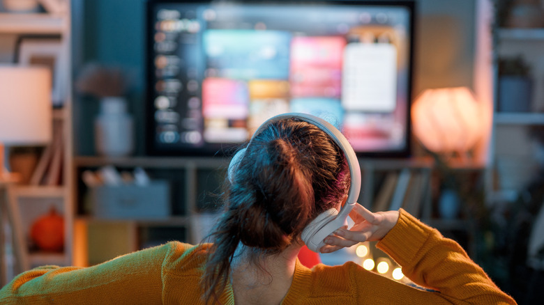 Woman wearing white headphones watching TV at home
