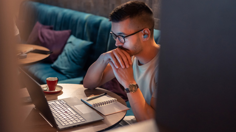 A man uses a laptop while wearing wireless earbuds.