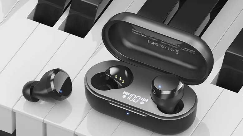 A pair of TOZO T12 earbuds with charging case, sitting on a piano keyboard.