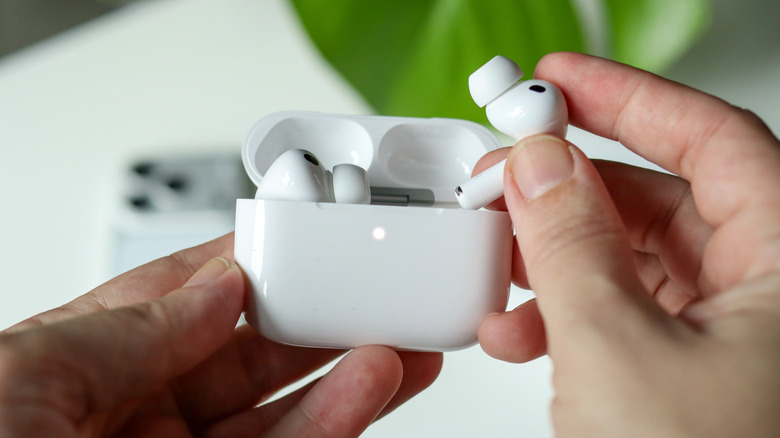 Holding the AirPods 3 and charging case with an iPhone in the background