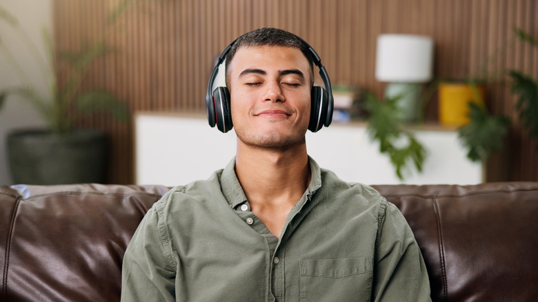 A person smiling with his eyes closed, wearing headphones and listening to music