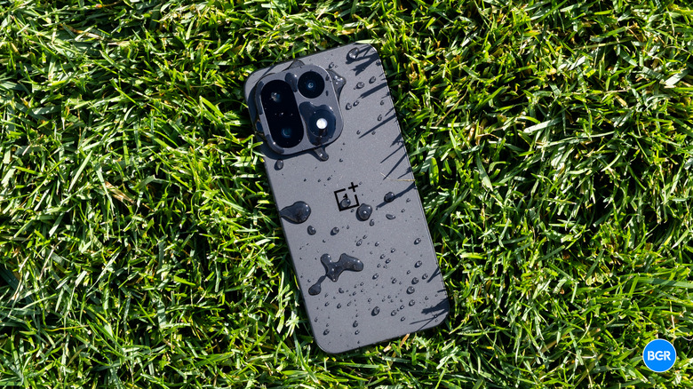 The OnePlus 15 dropped on grass, with water drops seen on the rear panel and camera.