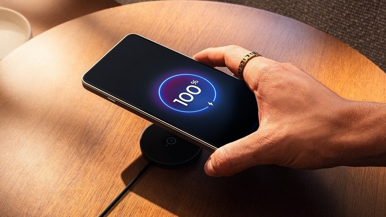 Close-up of a person picking up the Motorola Edge 70 Max with 100% battery level from a wireless charger