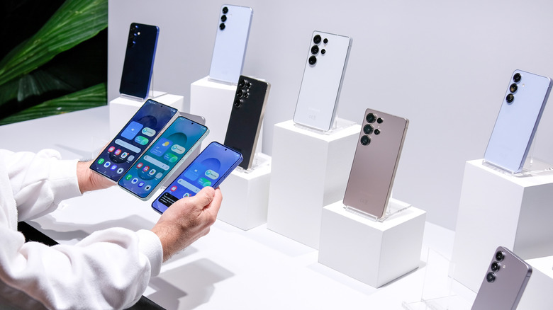 Samsung smartphones displayed on stands, with a person holding three phones in front of them.