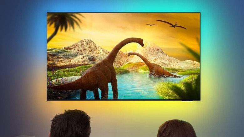 The Govee RGBIC Smart LED Strip Lights are attached to a wall-mounted TV. A family watches a dinosaur movie.