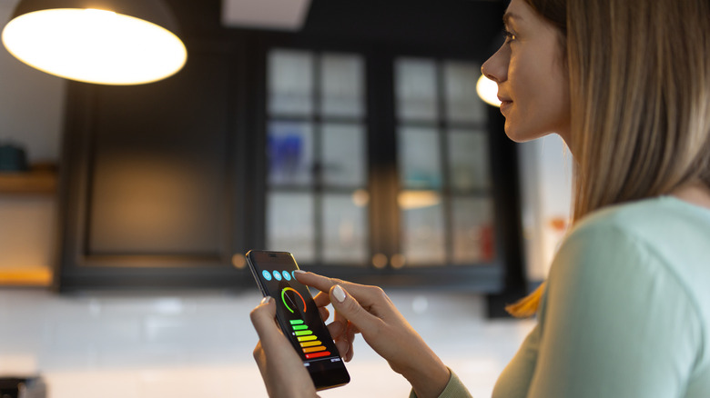A woman using a smartphone to control smart light bulbs.