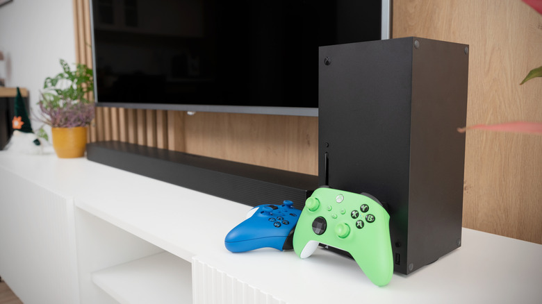 An Xbox Series X with the green and blue controller on a TV stand