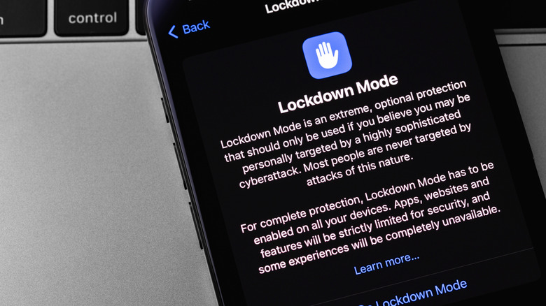 An iPhone with Lockdown Mode prompt on the screen is pictured.
