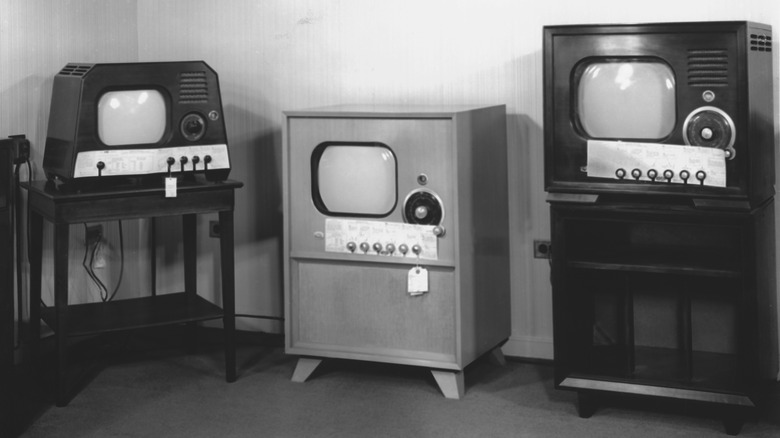 A black and white photo displaying an assortment of vintage console TV sets