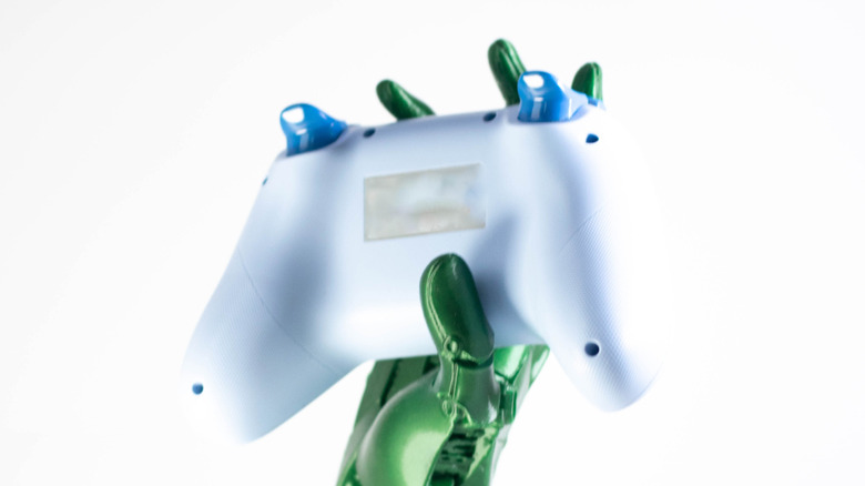 Back view of a white gaming controller held by a green robotic hand.