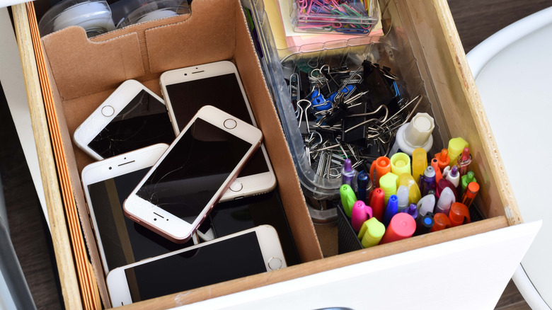 A drawer full of old smartphones and stationary supplies.