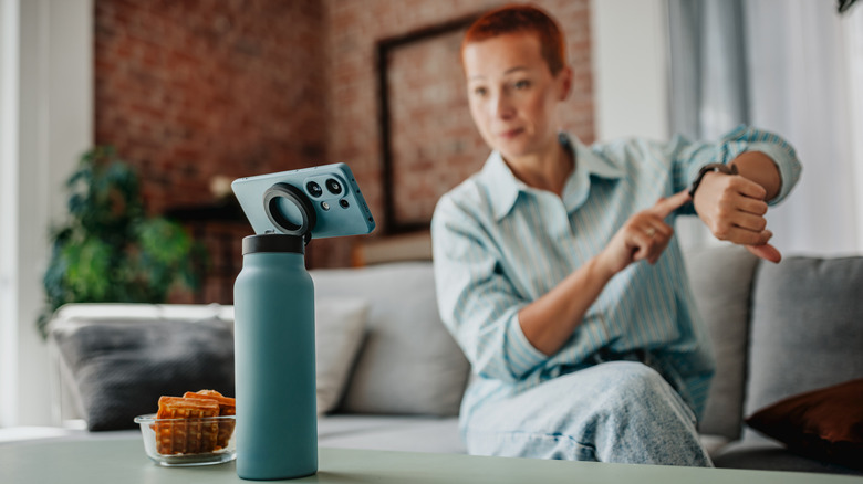 A woman looking at a propped-up smartphone on a table.
