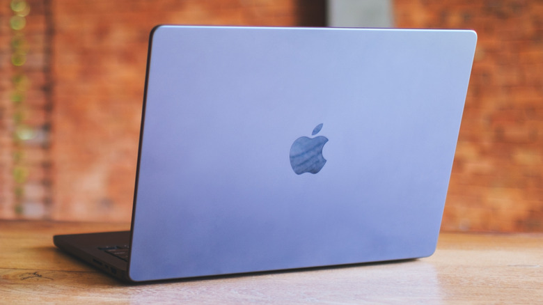 A MacBook sitting on a wooden table against a brick background