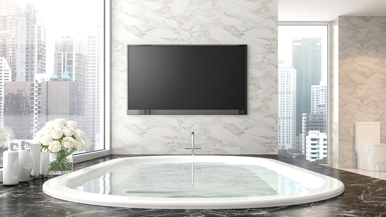 A TV mounted above a bathtub in a large bathroom