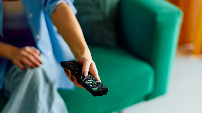 A person holding a TV remote while sitting on a sofa