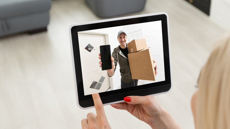 A woman holding a tablet showing a deliveryman with packages.