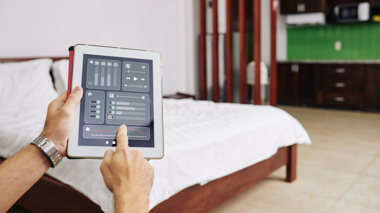 Hands in a bedroom using a tablet as a smart home controller.