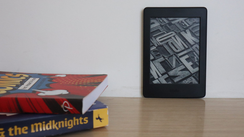 An Amazon Kindle against a wall with books on the side.