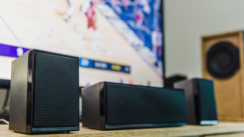 Three speakers in front of a TV in the background.