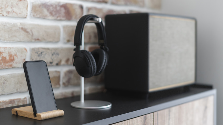 A vintage style speaker beside wireless headphones on a stand and smartphone.