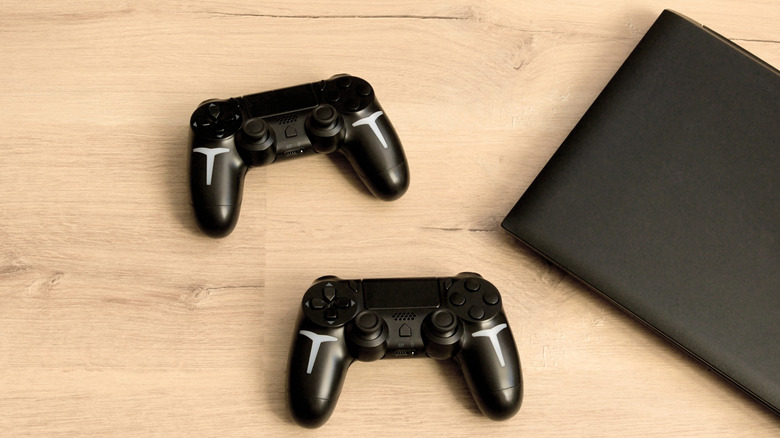 two gaming controllers and a laptop on a wooden desk