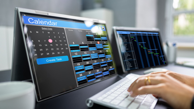 Hand typing on keyboard with two screens in front