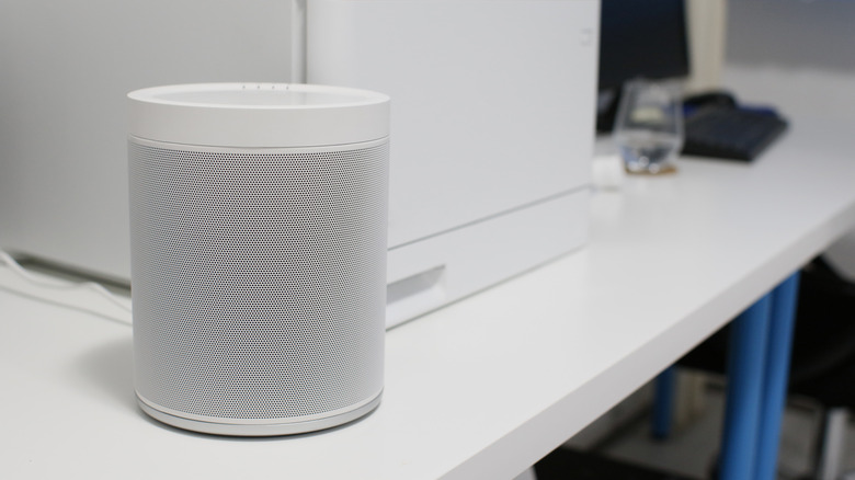 White smart speaker placed on a desk next to a computer monitor.
