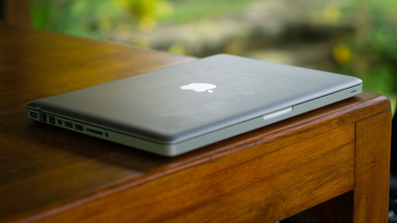 An old MacBook closed on  the corner of a wooden desk