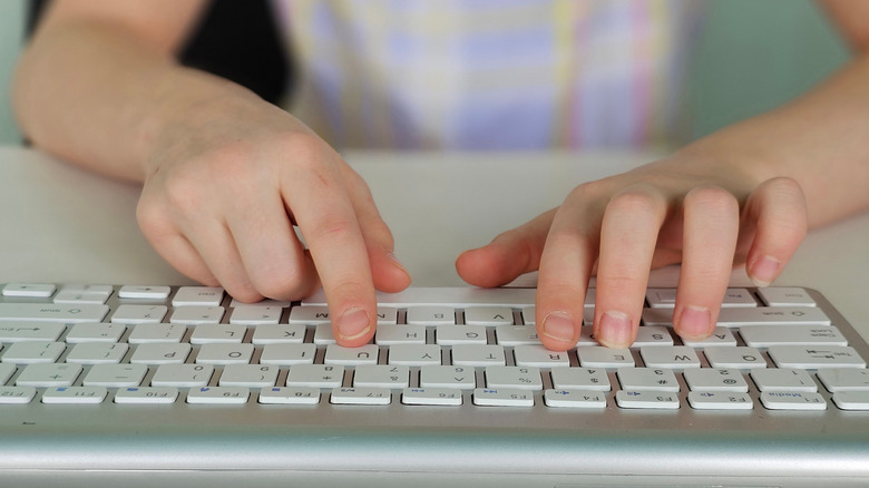 A close-up of a child's hands typing away on a silver keyboard with white keys