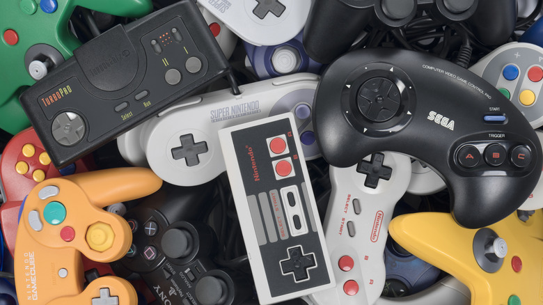 Several game controllers sitting in a pile, including controllers from Nintendo and Sega consoles such as the SNES, Nintendo 64, and more