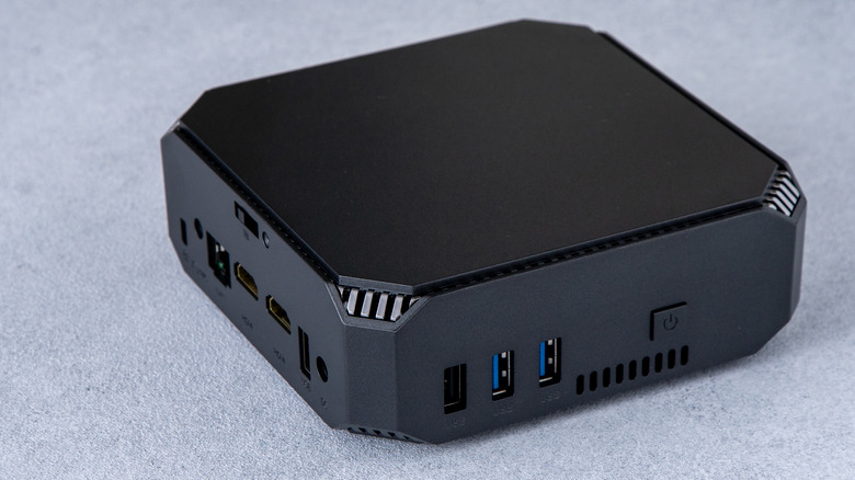 A black mini PC sits on what appears to be a blue, carpeted surface, the image showcases the device's numerous ports