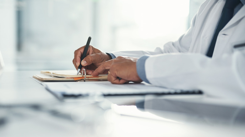A person in a white lab coat writing on a clipboard