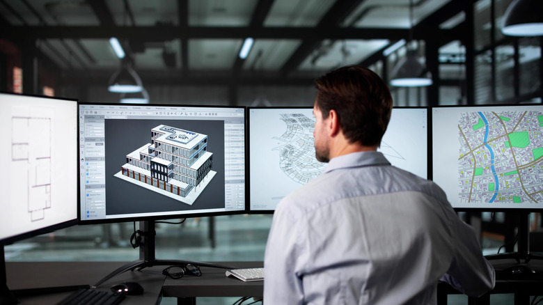 A man in an office looking at multiple monitors in front of him