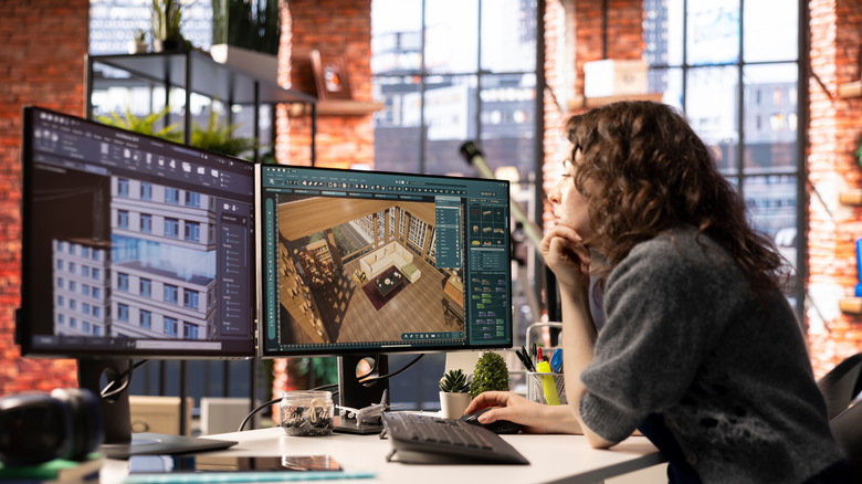 A person looking at their PC with two monitors open. One displays an internal view of a house, while the other shows the same place from the outside