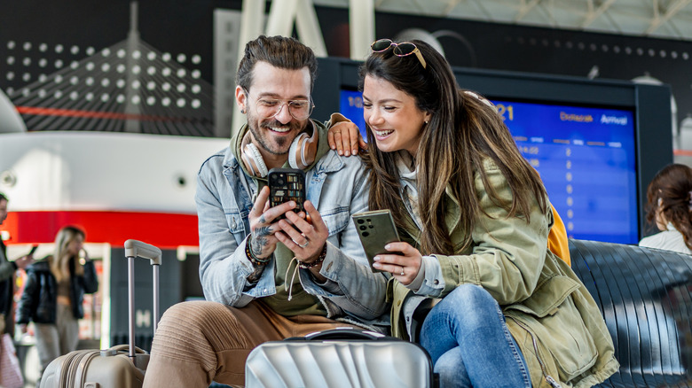 A couple at the airport showing each other content on their smatphones