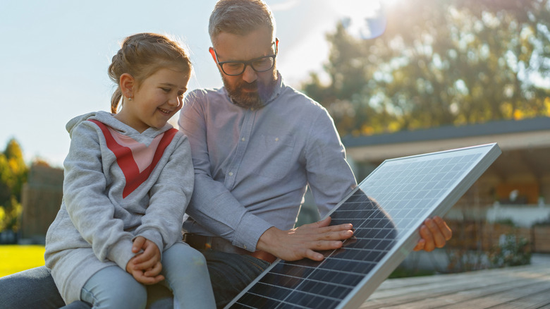 A father showing his daughter a solar panel in the yard.