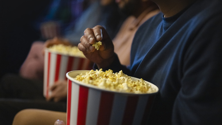 People holding buckets of popcorn while they watch a movie.
