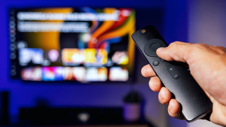 A person pointing a Fire TV remote toward a blurred TV screen.
