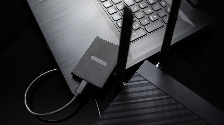 laptop, external storage drive, and router placed on a black desk