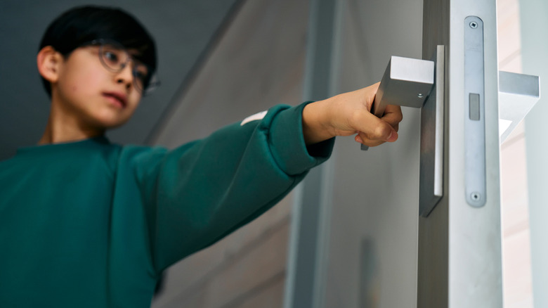 Young boy opening a door to a home that leads outside.