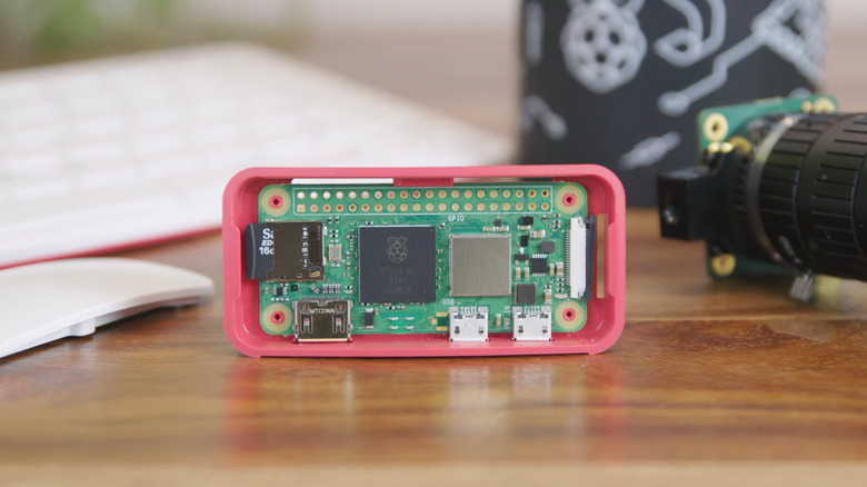 A Raspberry Pi Zero 2 W, in a case, placed on a table with a camera module beside it.