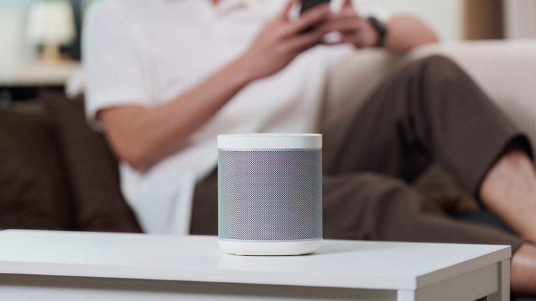 Smart speaker on a table with a person using a phone in the background.