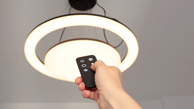 Hand using a remote control to adjust a ceiling light.