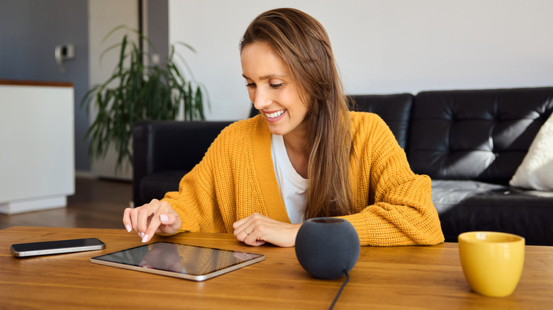 Woman using a tablet beside a smart speaker at home.
