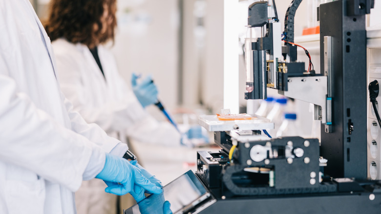 2 people wearing protective gear while operating a 3D printer