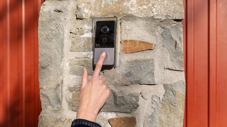 A hand pressing a button on a video doorbell