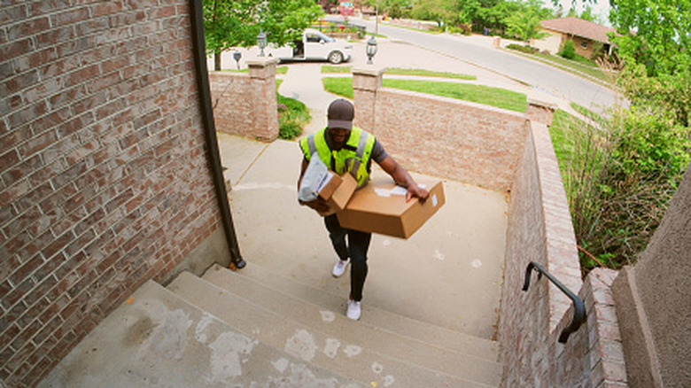 A delivery person carrying packages to a door seen from a security camera